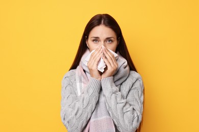 Sick woman with tissue on orange background. Cold symptoms