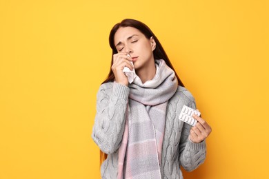 Sick woman with tissue and pills on orange background. Cold symptoms