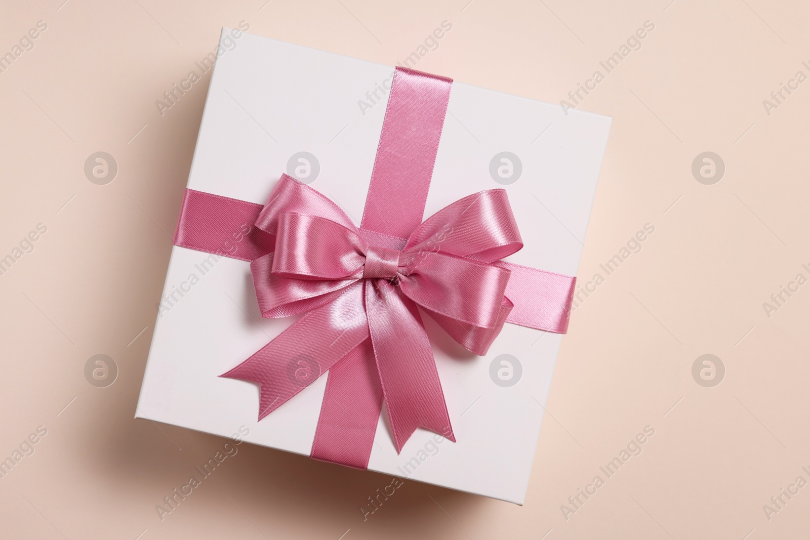 Photo of Gift box with bow on beige background, top view