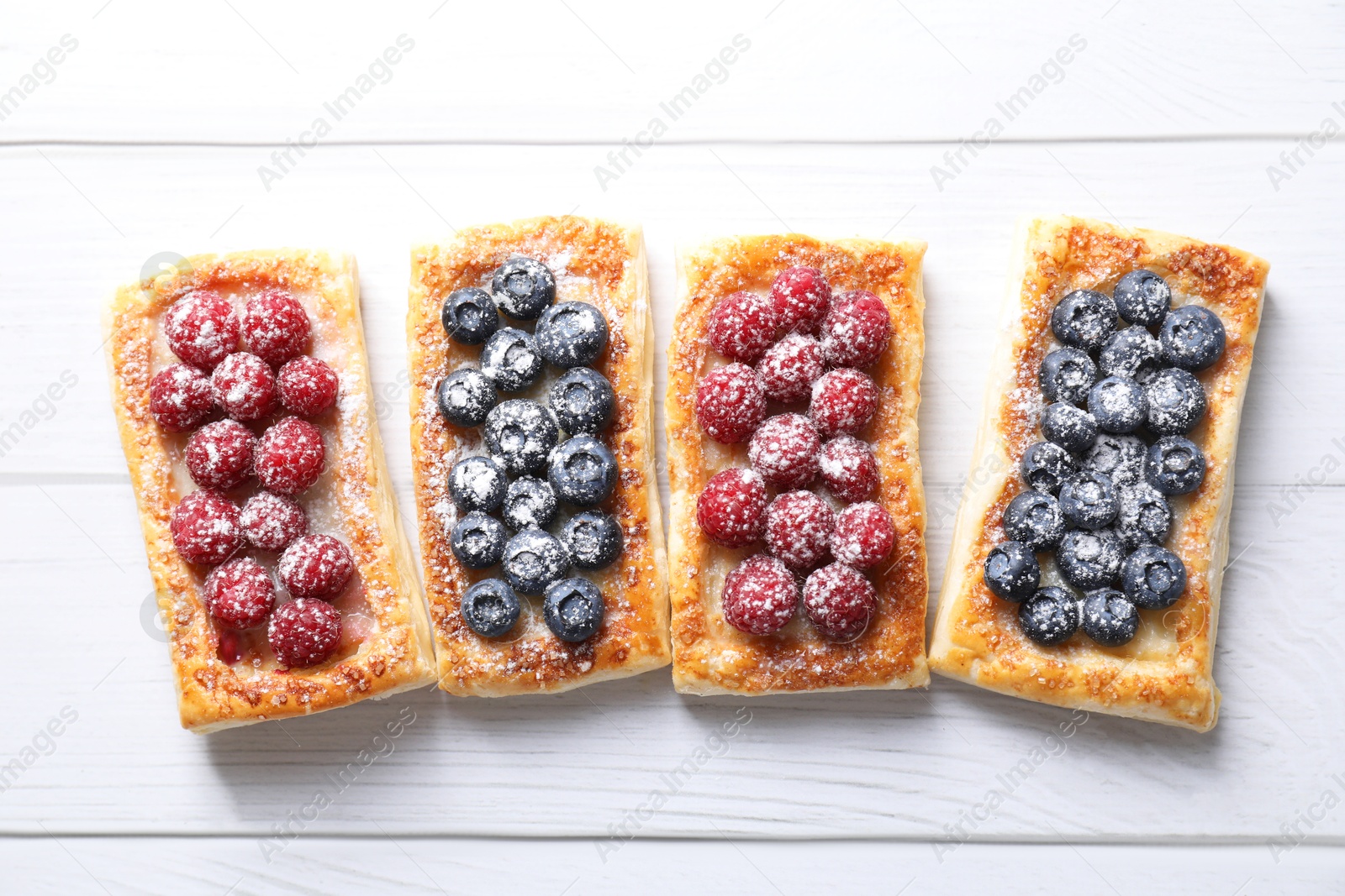 Photo of Tasty puff pastries with berries on white wooden table, flat lay