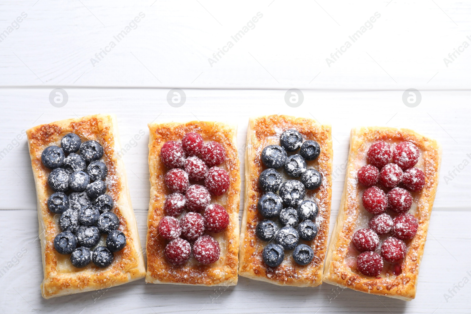 Photo of Tasty puff pastries with berries on white wooden table, flat lay. Space for text