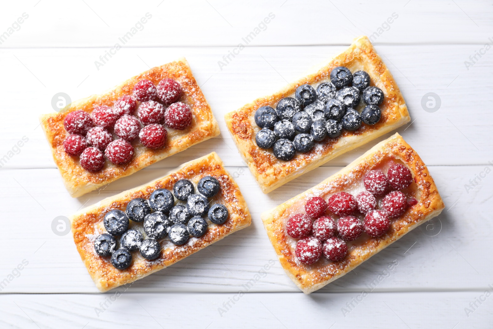 Photo of Tasty puff pastries with berries on white wooden table, flat lay