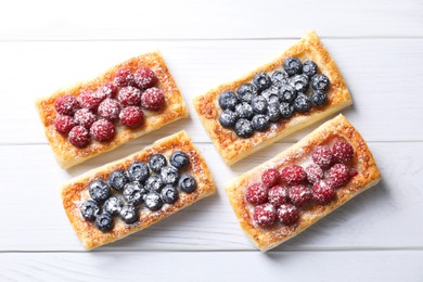 Tasty puff pastries with berries on white wooden table, flat lay