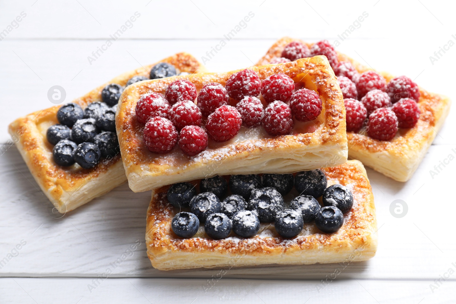 Photo of Tasty puff pastries with berries on white wooden table, closeup