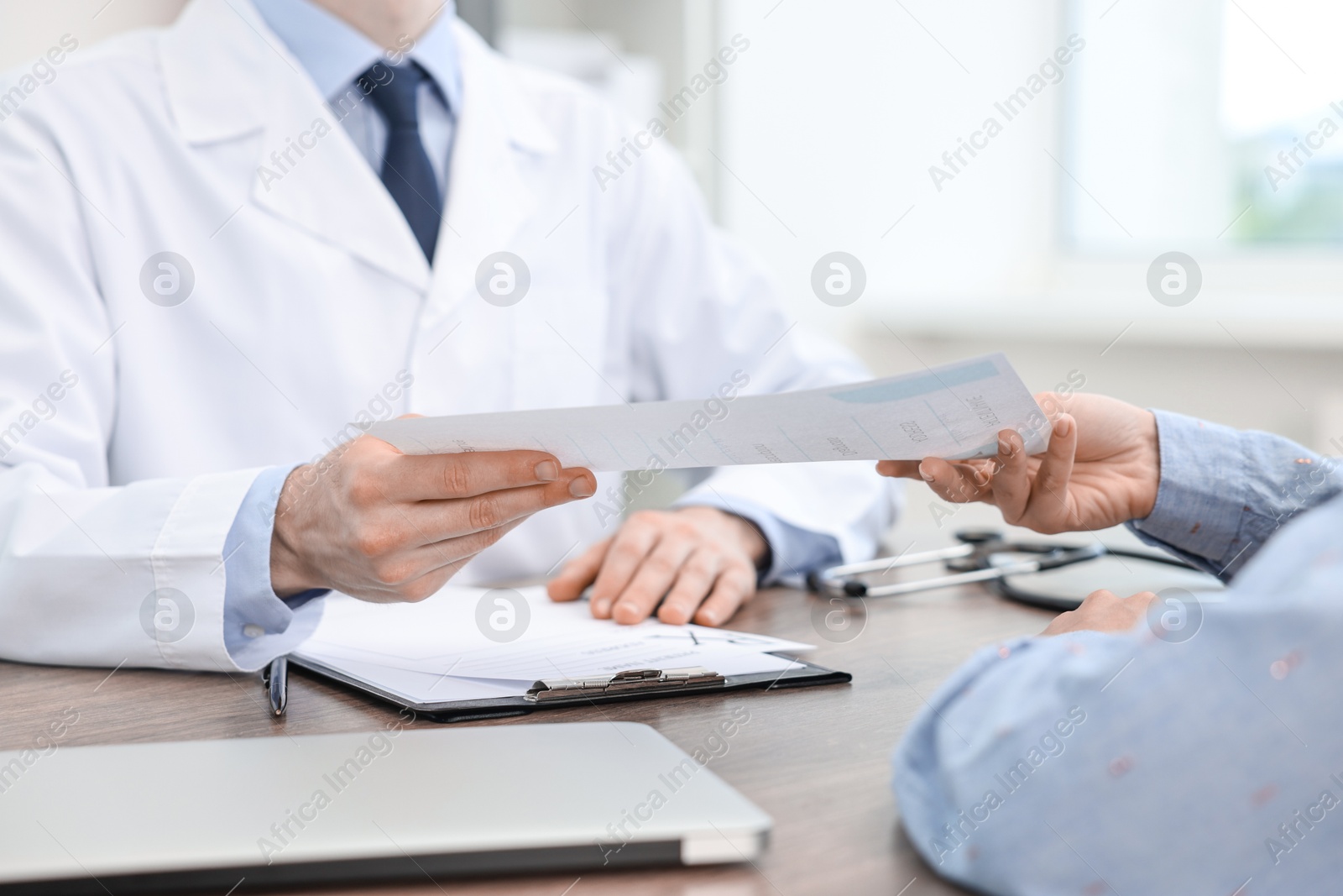 Photo of Doctor giving prescription to patient at wooden table in clinic, closeup