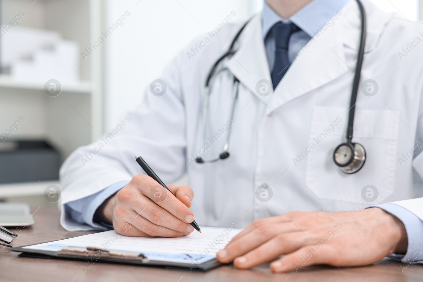 Photo of Doctor writing prescription at wooden table in clinic, closeup