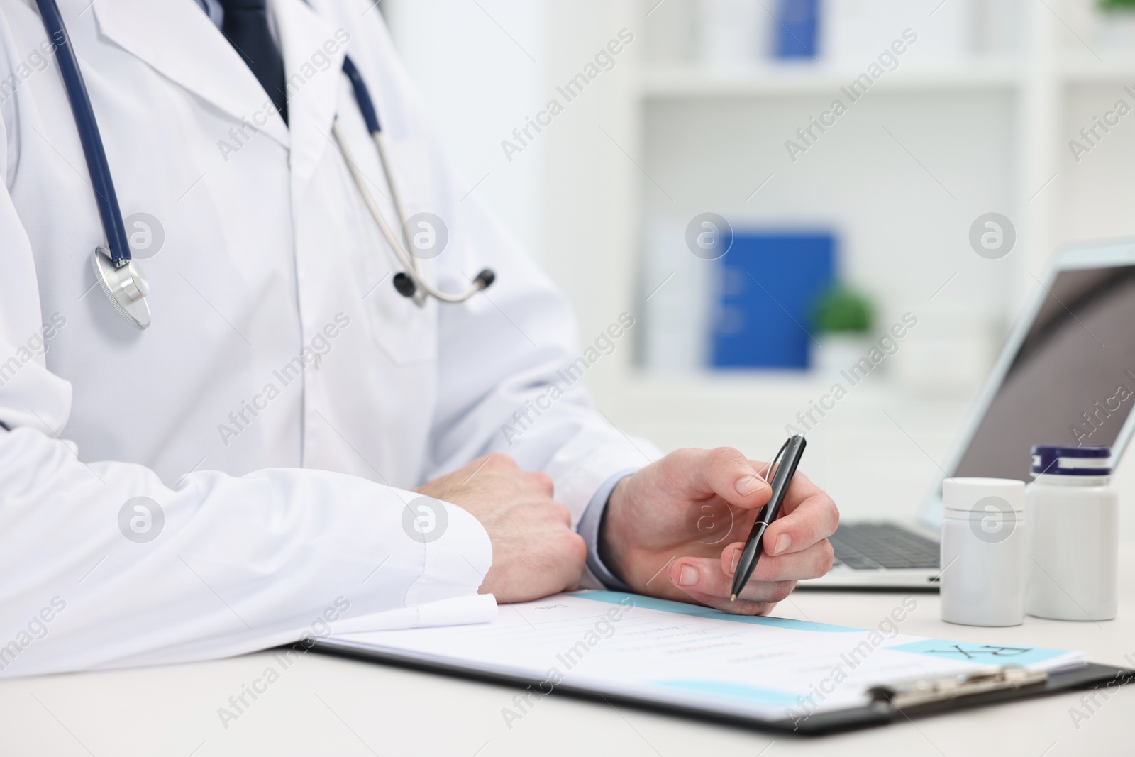 Photo of Doctor writing prescription at white table in clinic, closeup