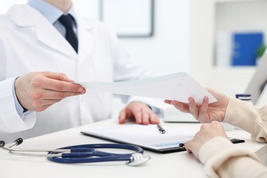 Photo of Doctor giving prescription to patient at white table in clinic, closeup