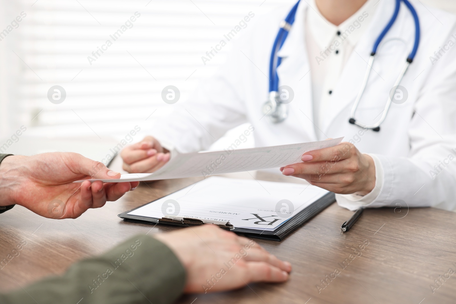 Photo of Doctor giving prescription to patient at wooden table in clinic, closeup