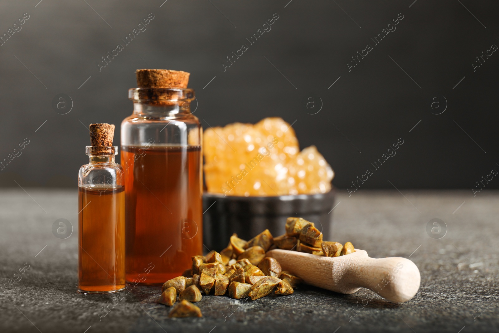 Photo of Honey tincture and scoop with propolis granules on grey textured table, closeup. Alternative medicine