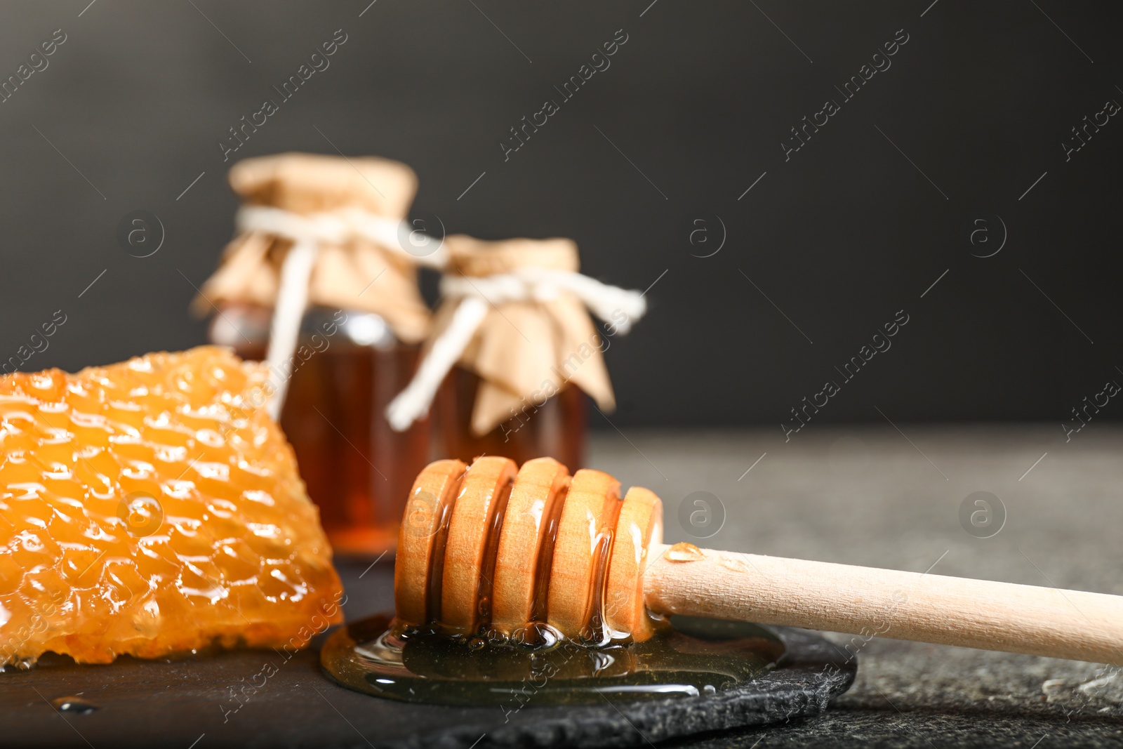 Photo of Honeycomb, dipper and honey tincture on grey textured table, closeup. Alternative medicine