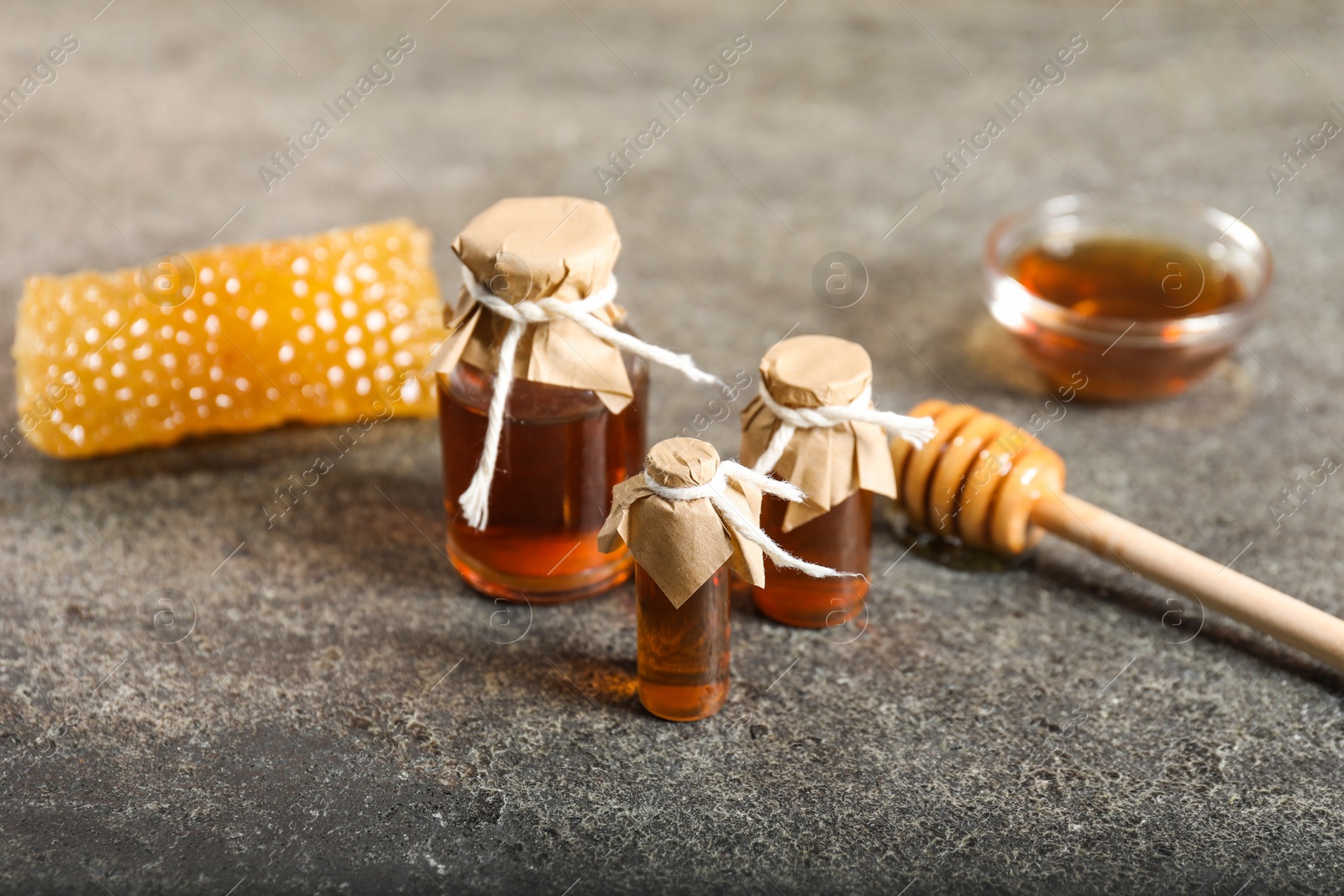 Photo of Honey tinctures, dipper and honeycomb on grey textured table, closeup. Alternative medicine