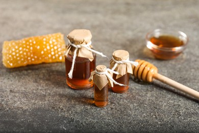 Honey tinctures, dipper and honeycomb on grey textured table, closeup. Alternative medicine