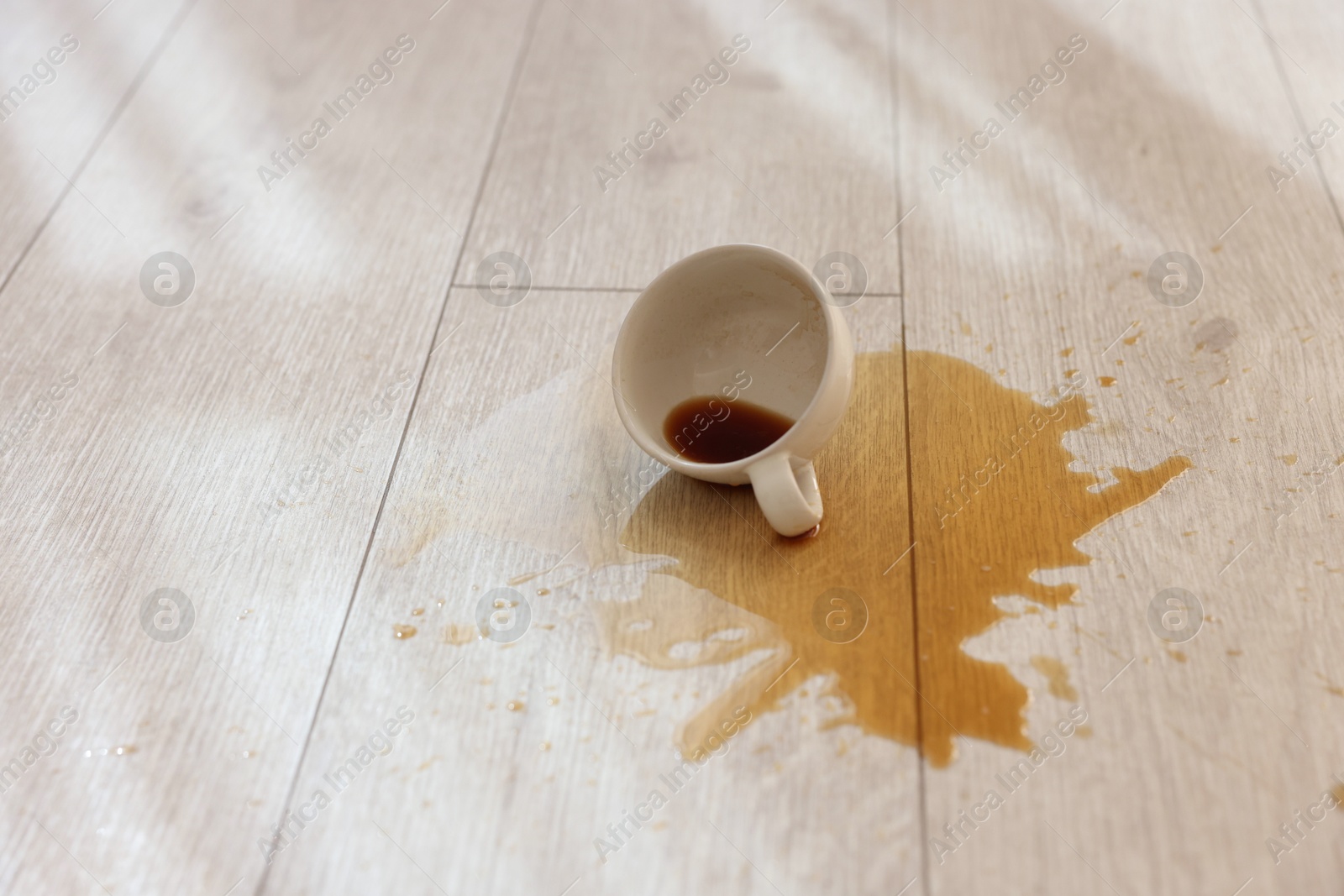 Photo of Cup with spilled drink on wooden floor