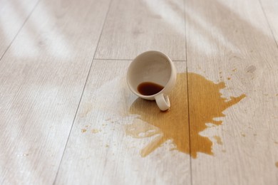 Photo of Cup with spilled drink on wooden floor