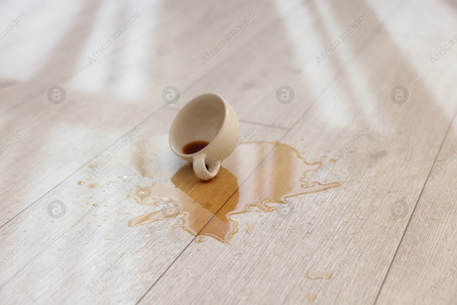 Photo of Cup with spilled drink on wooden floor