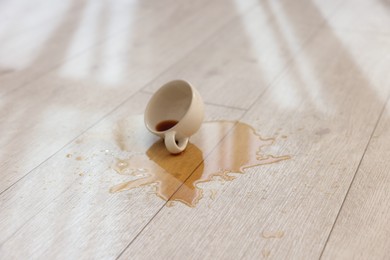 Photo of Cup with spilled drink on wooden floor