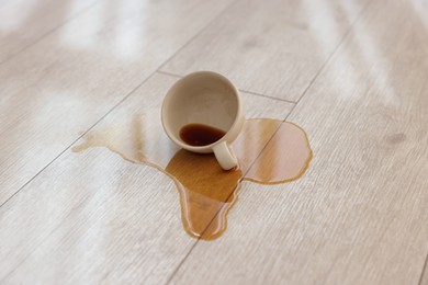 Photo of Cup with spilled drink on wooden floor, closeup