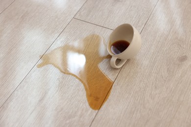 Photo of Cup with spilled drink on wooden floor