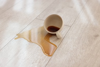 Cup with spilled drink on wooden floor