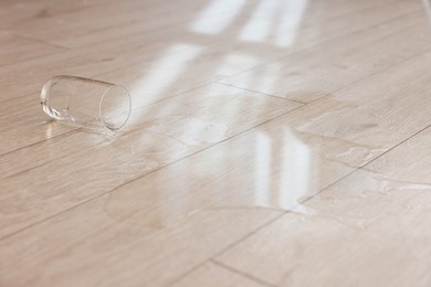 Photo of Glass with spilled drink on wooden floor