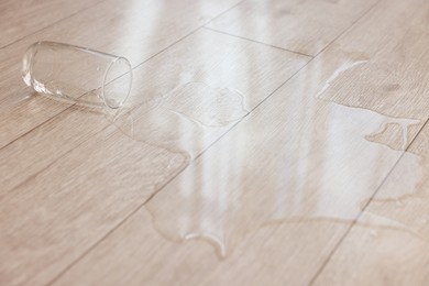 Glass with spilled drink on wooden floor, closeup