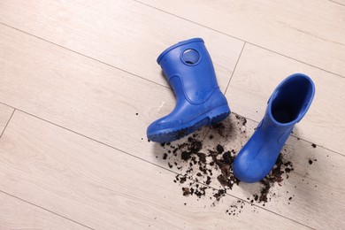 Photo of Rubber boots with mud on wooden floor, top view. Space for text