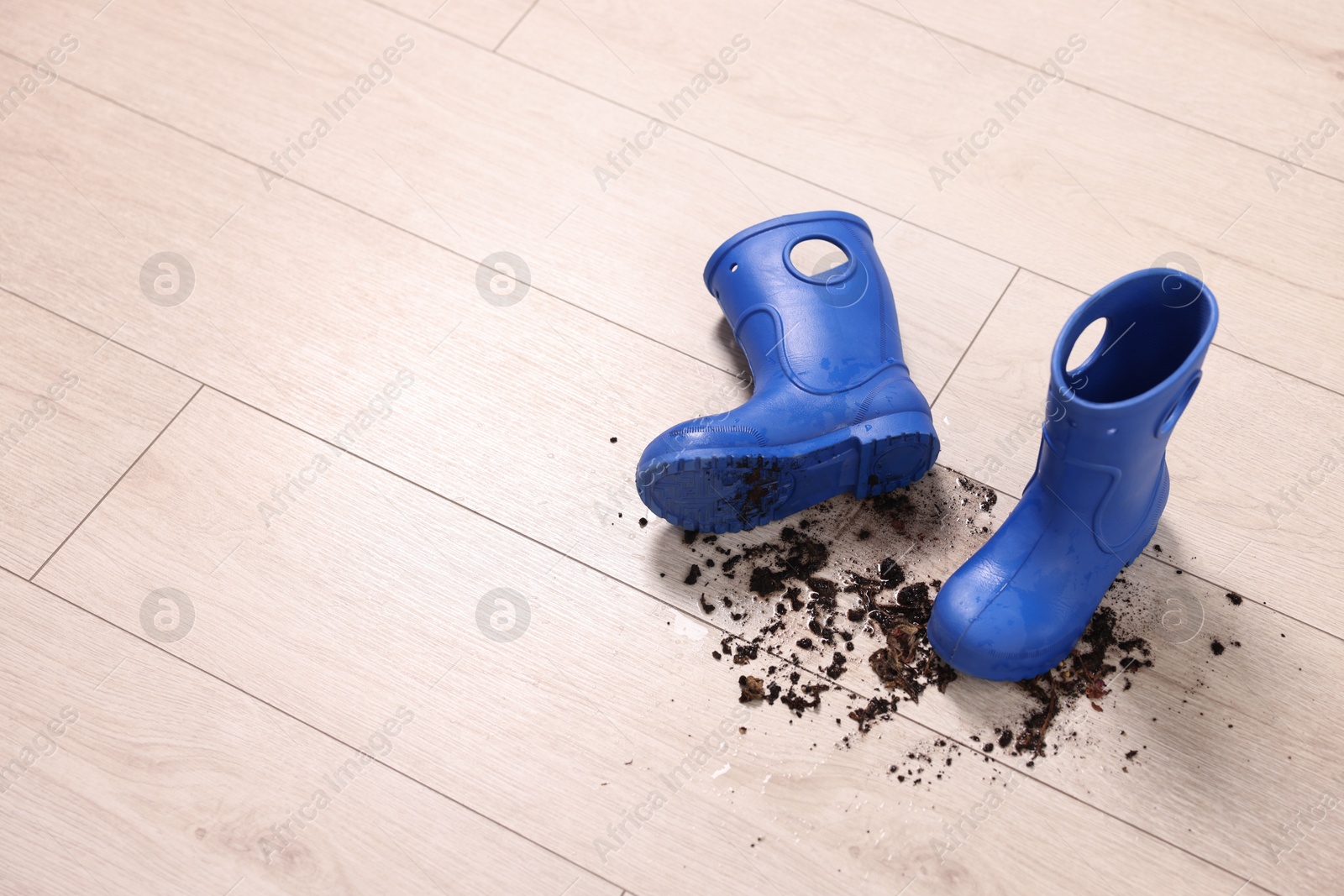 Photo of Rubber boots with mud on wooden floor. Space for text