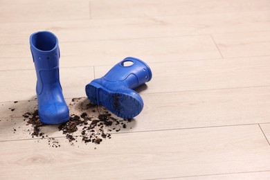 Photo of Rubber boots with mud on wooden floor. Space for text