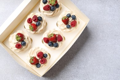 Photo of Tasty cupcakes with different berries in box on light grey table, top view. Space for text