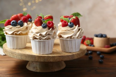 Photo of Tasty cupcakes with different berries and mint on wooden table, closeup