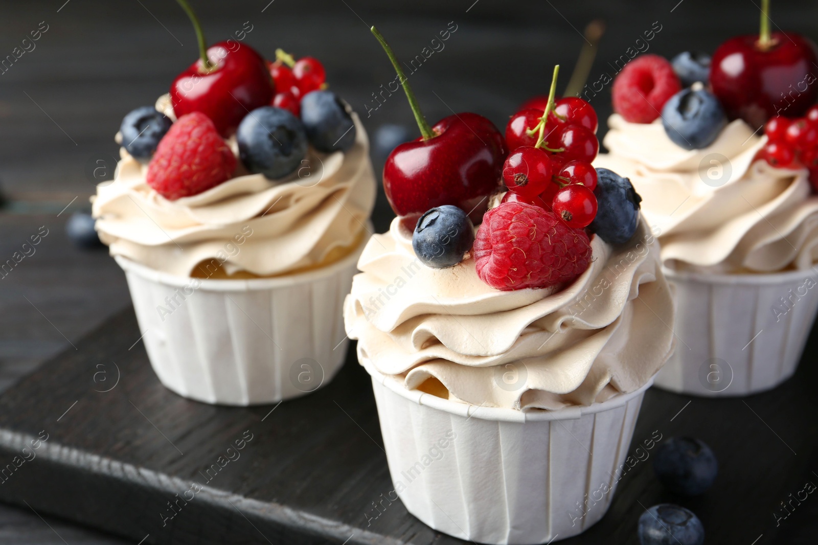 Photo of Tasty cupcakes with different berries on black wooden table, closeup