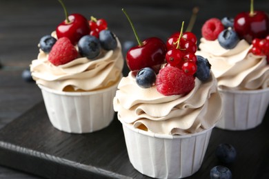 Photo of Tasty cupcakes with different berries on black wooden table, closeup