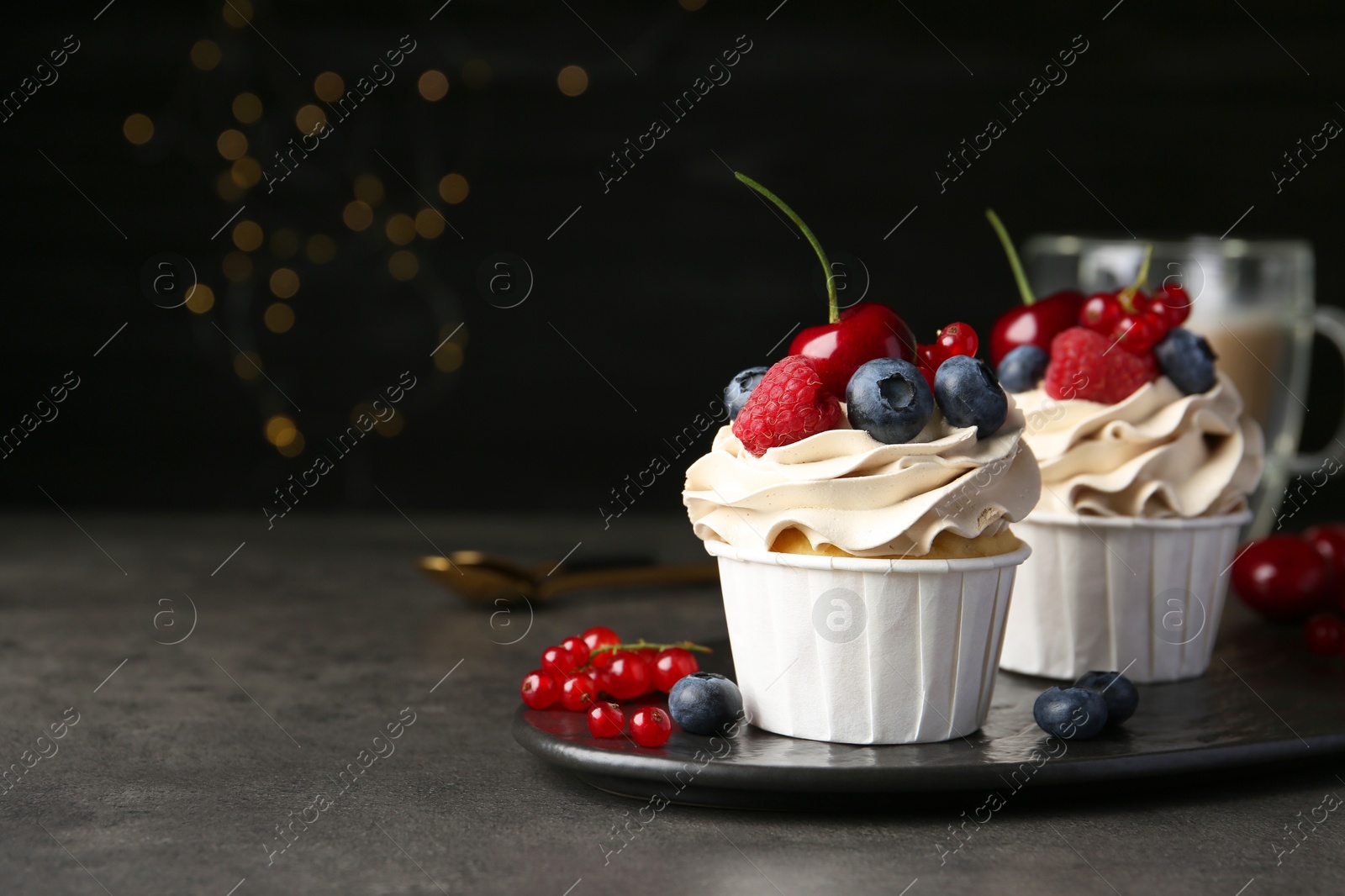 Photo of Tasty cupcakes with different berries on grey table, closeup. Space for text