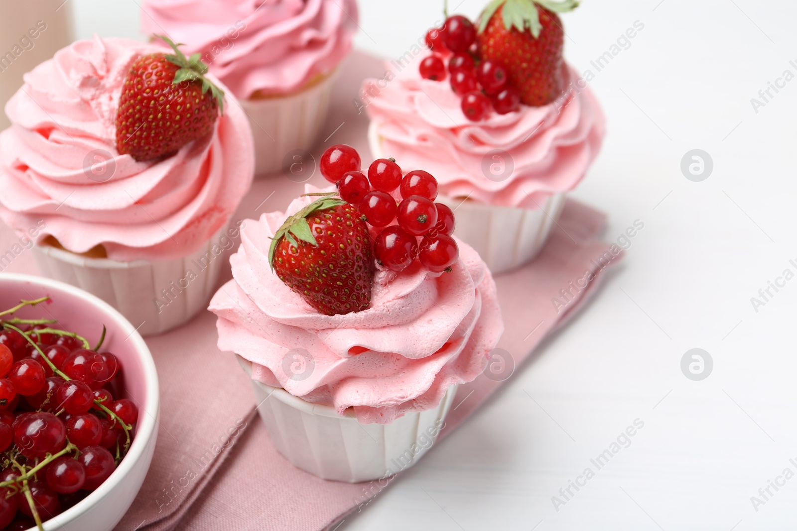 Photo of Tasty cupcakes with strawberries and red currants on white table, closeup. Space for text