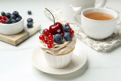 Photo of Tasty cupcake with different berries and tea on white marble table