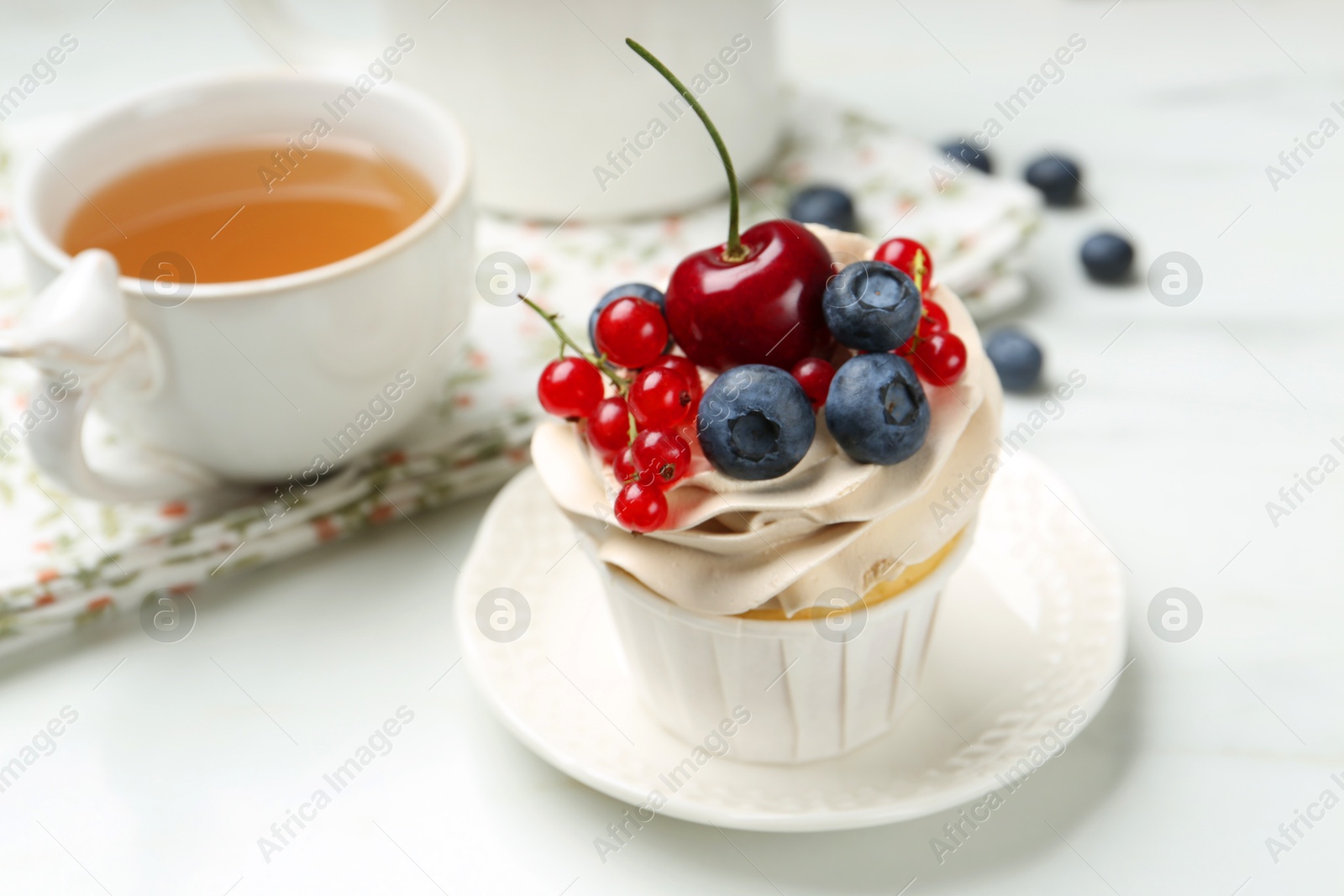 Photo of Tasty cupcake with different berries and tea on white marble table, closeup