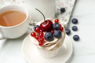 Photo of Tasty cupcake with different berries and tea on white marble table, closeup