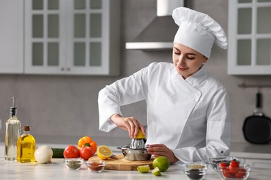 Woman squeezing juice out of lemon at white marble table in kitchen