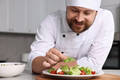 Photo of Professional chef decorating delicious salad with basil at table in kitchen