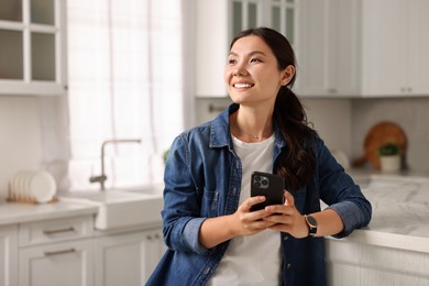 Smiling woman with smartphone in kitchen. Space for text