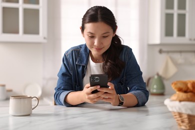 Beautiful woman using smartphone at table in kitchen