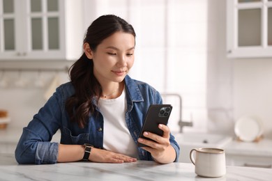 Beautiful woman using smartphone at table in kitchen