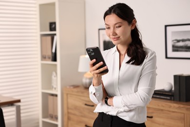 Beautiful businesswoman with smartphone in office. Space for text