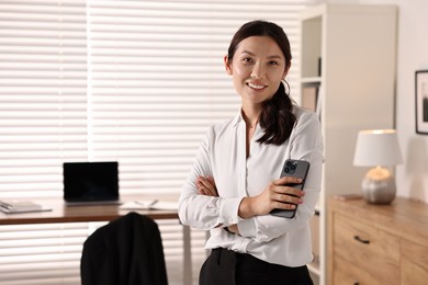 Smiling businesswoman with smartphone in office. Space for text