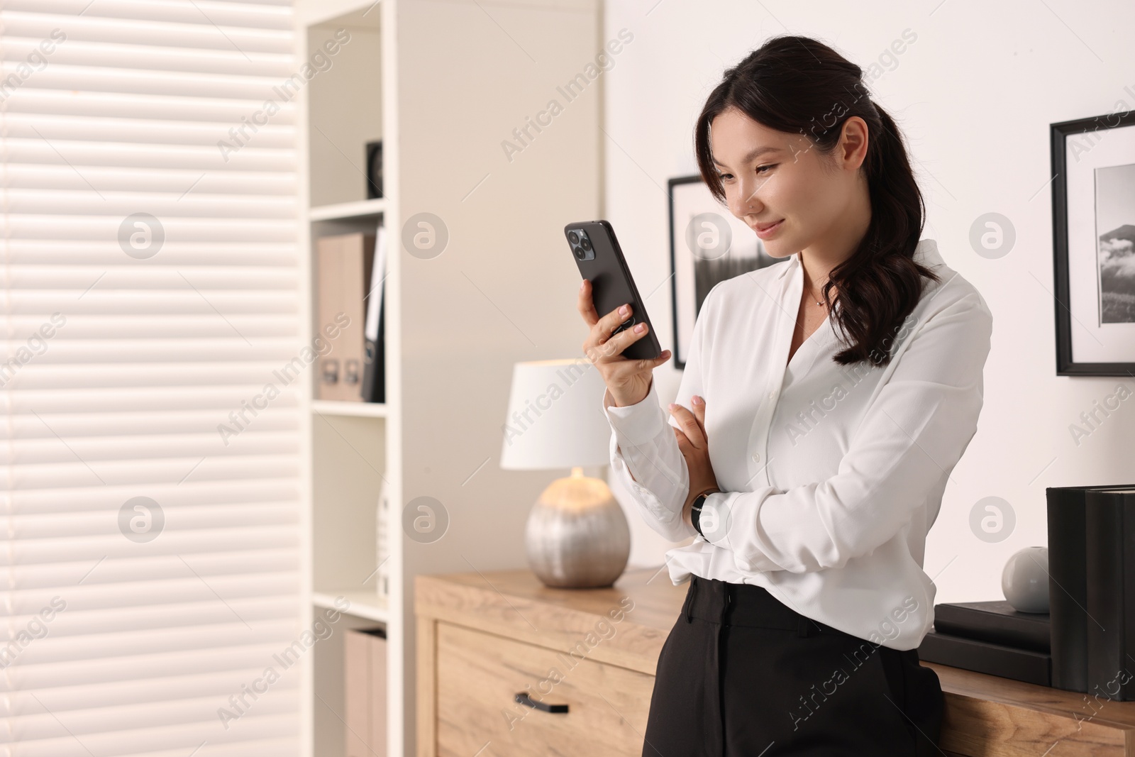 Photo of Beautiful businesswoman using smartphone in office. Space for text