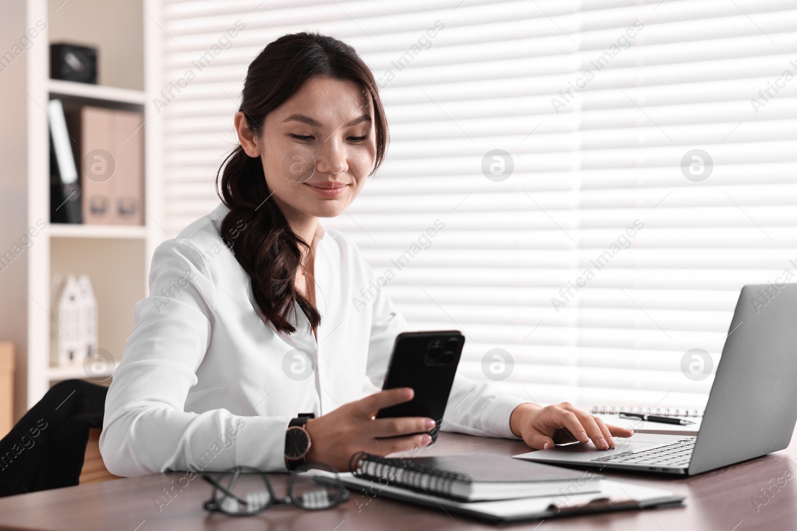 Photo of Beautiful young businesswoman using smartphone in office