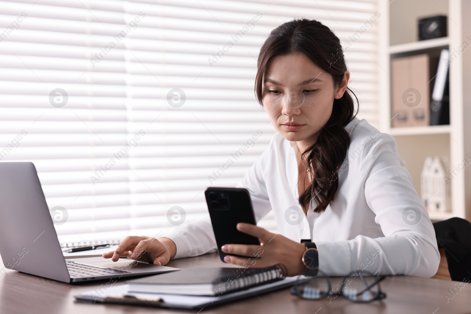 Photo of Beautiful young businesswoman using smartphone in office