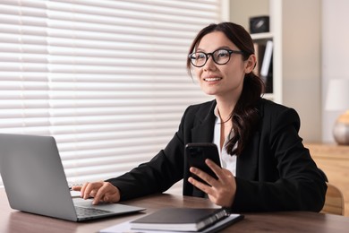 Photo of Smiling businesswoman with smartphone at table in office