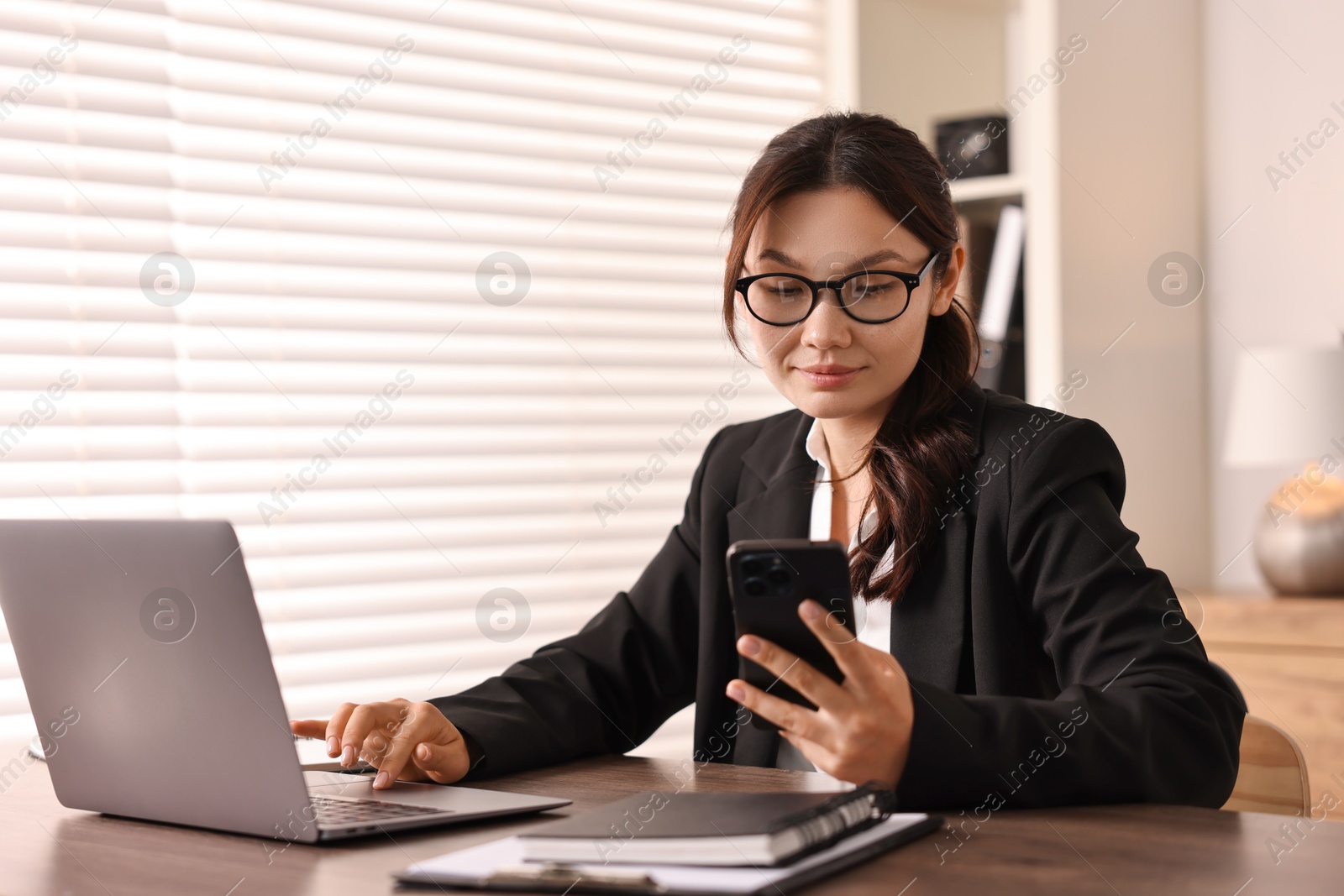 Photo of Beautiful businesswoman with smartphone at table in office